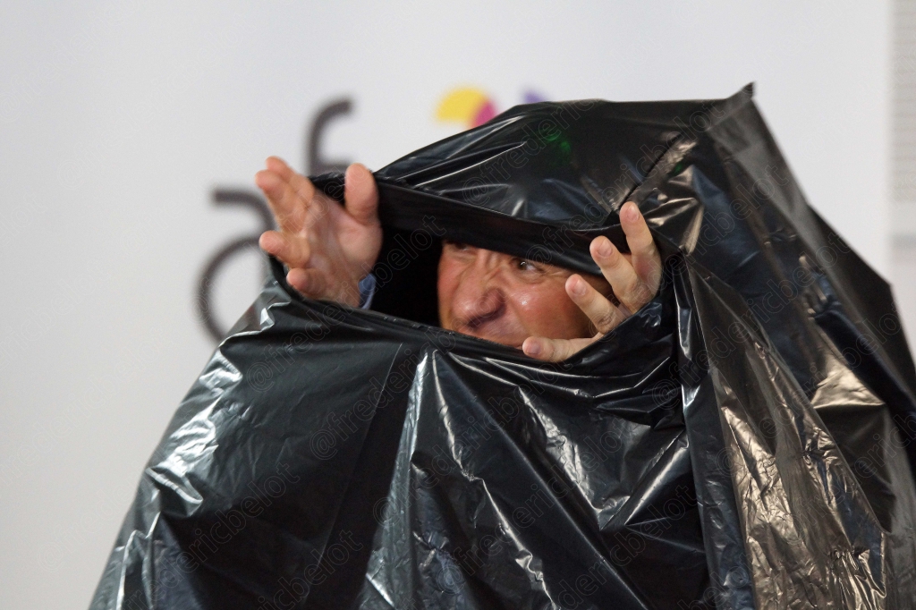 Homme en costume se cachant la tête sous un sac plastique noir, bras levés