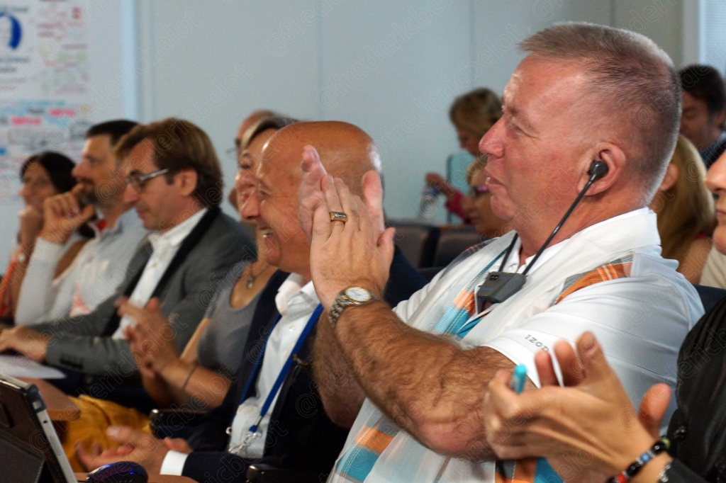 Groupe de participants souriants et applaudissant, dont un homme avec micro-casque