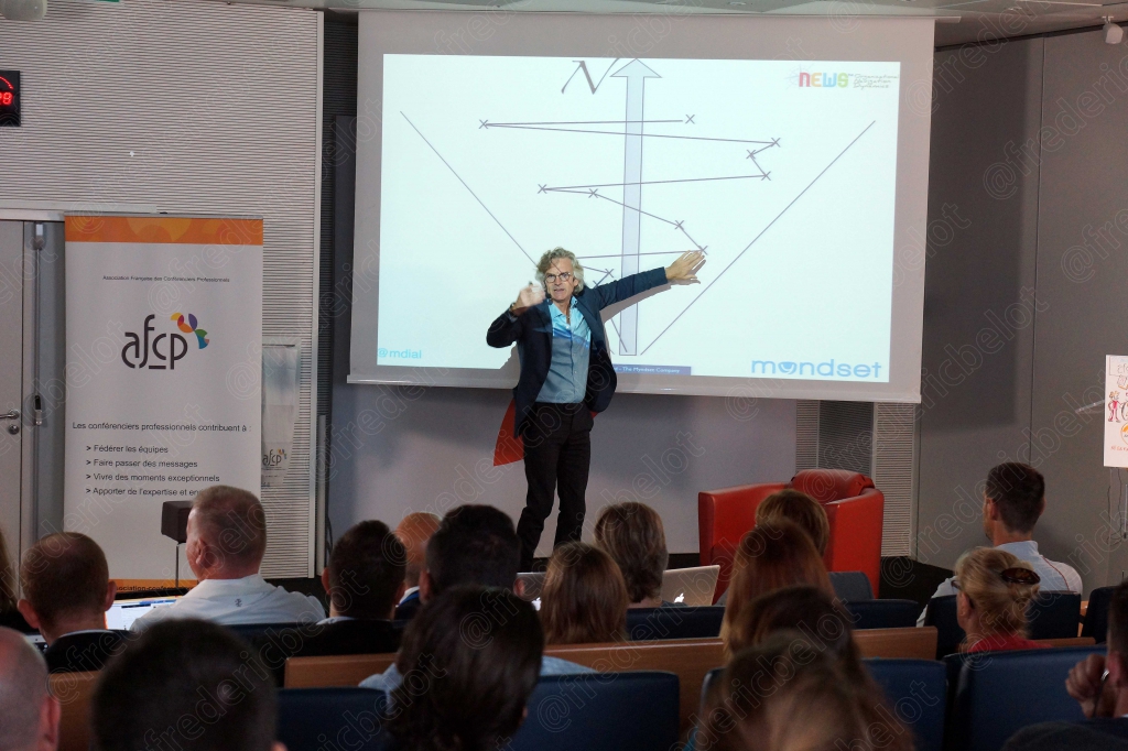 Femme sur scène pointant du doigt un graphique projeté à l'écran