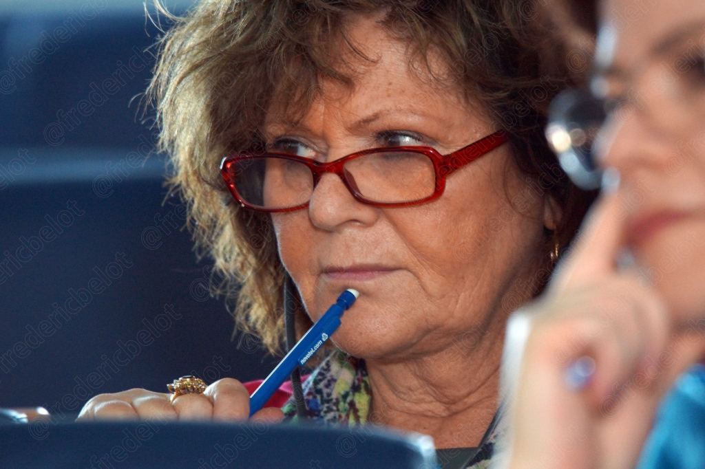 Femme à lunettes rouges tenant un stylo à la bouche, attentive