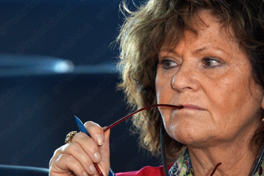 Femme aux cheveux gris tenant ses lunettes à la bouche, pensive