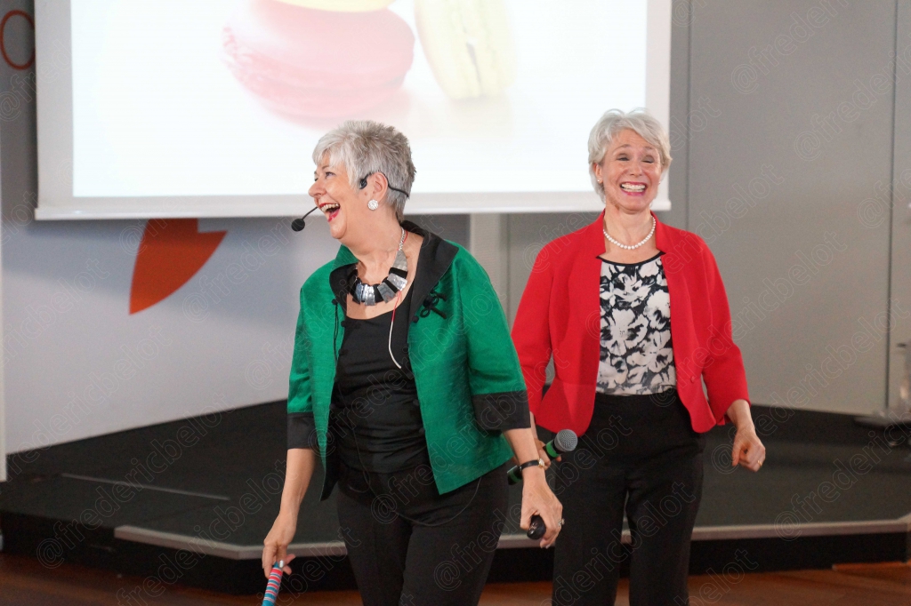 Deux femmes en veste verte et rouge riant sur scène, écran de mind-mapping en fond