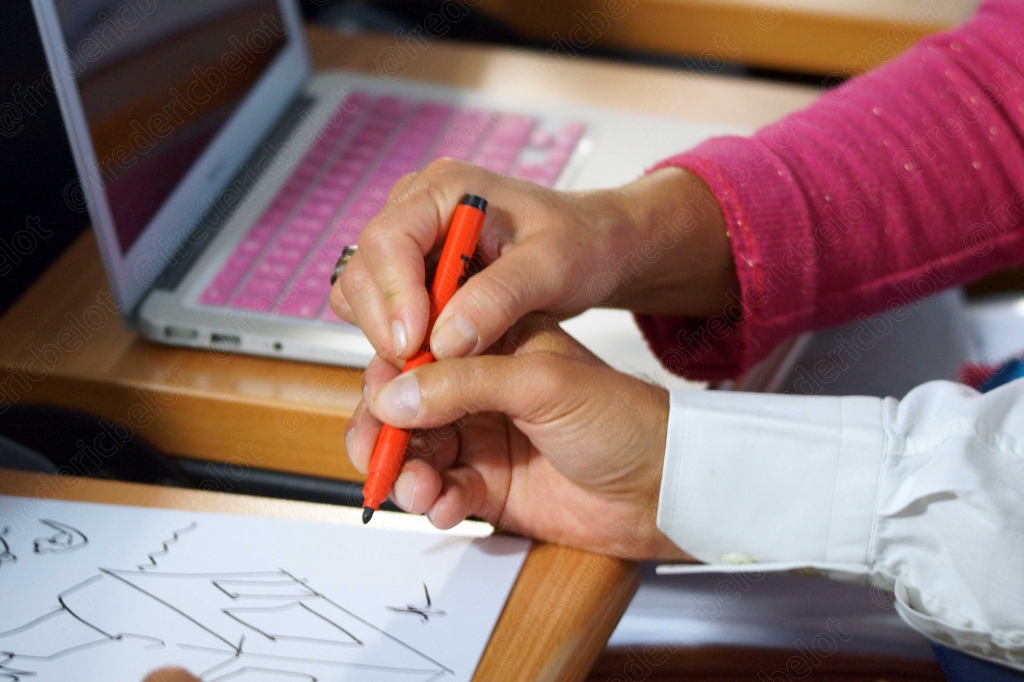 Gros plan sur une main tenant un stylo orange, dessinant un schéma