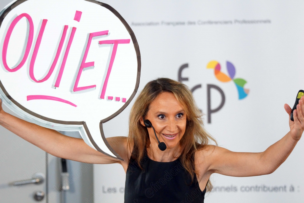 Femme blonde bras levés tenant une pancarte « OUI ET... » devant un kakémono afcp