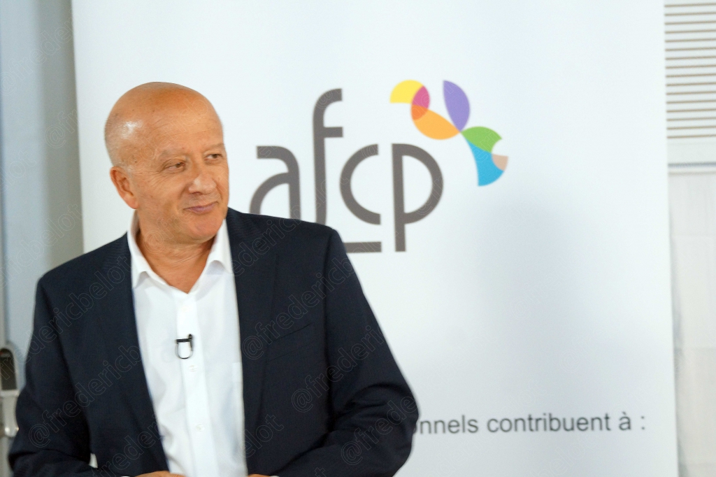 Homme chauve en costume parlant devant un écran affichant le logo afcp