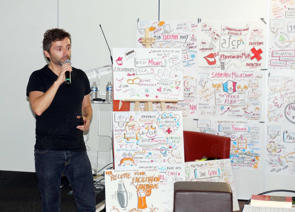 Homme en t-shirt noir parlant au micro devant un mur de mind-mapping