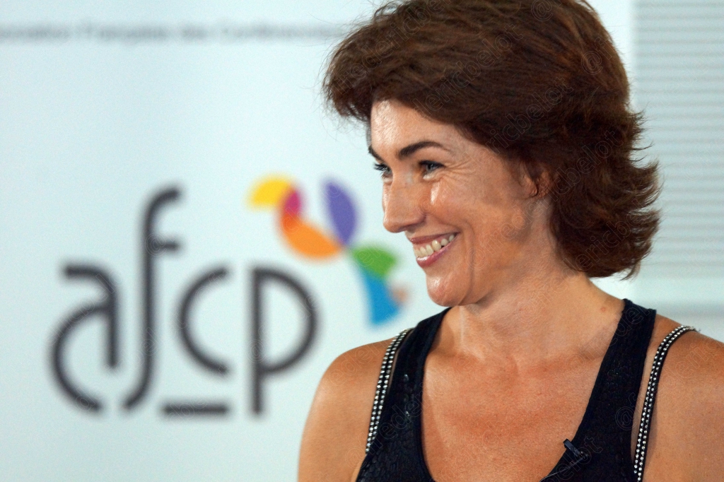 Femme aux cheveux bruns courts souriante devant le logo afcp