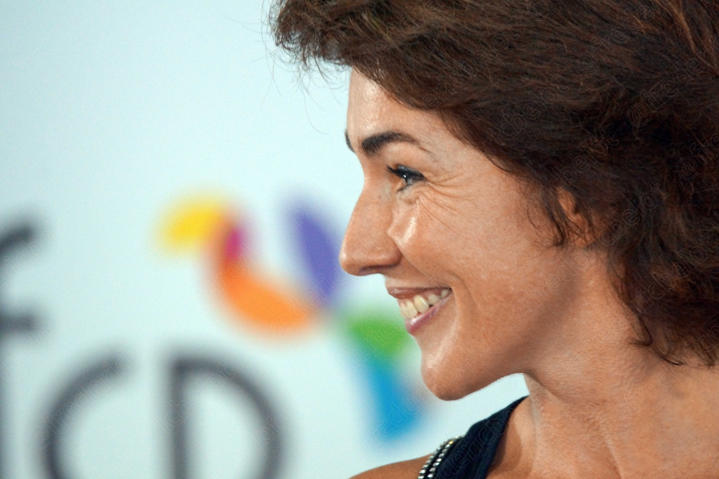 Femme aux cheveux bruns courts riant, de profil, devant le logo afcp