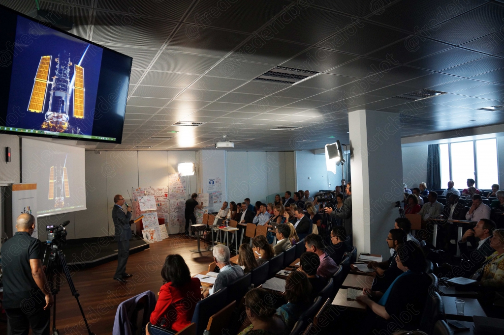 Salle de conférence, écran affichant une image de la Terre depuis l'espace, public de dos