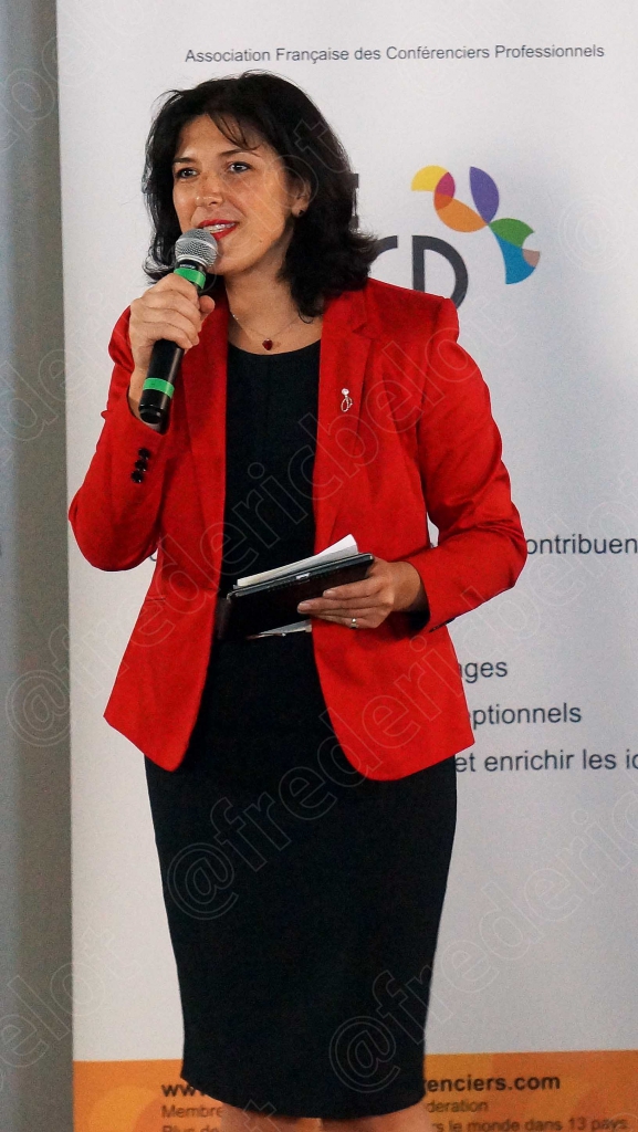 Femme en veste rouge parlant au micro devant un kakémono afcp, fond sombre