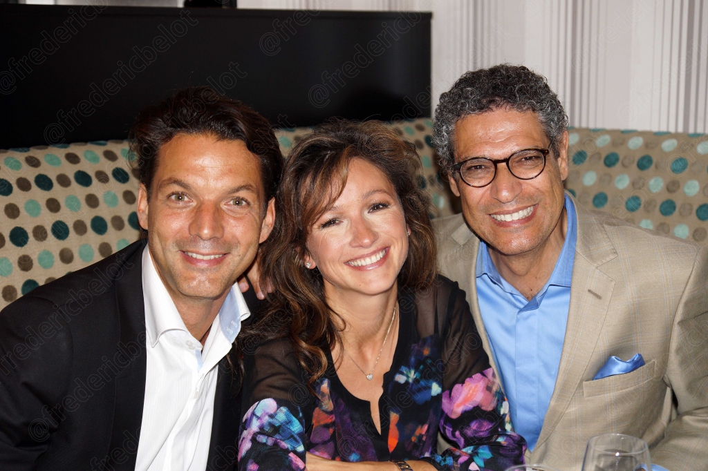 Trois convives souriants posent ensemble à table dans un restaurant.