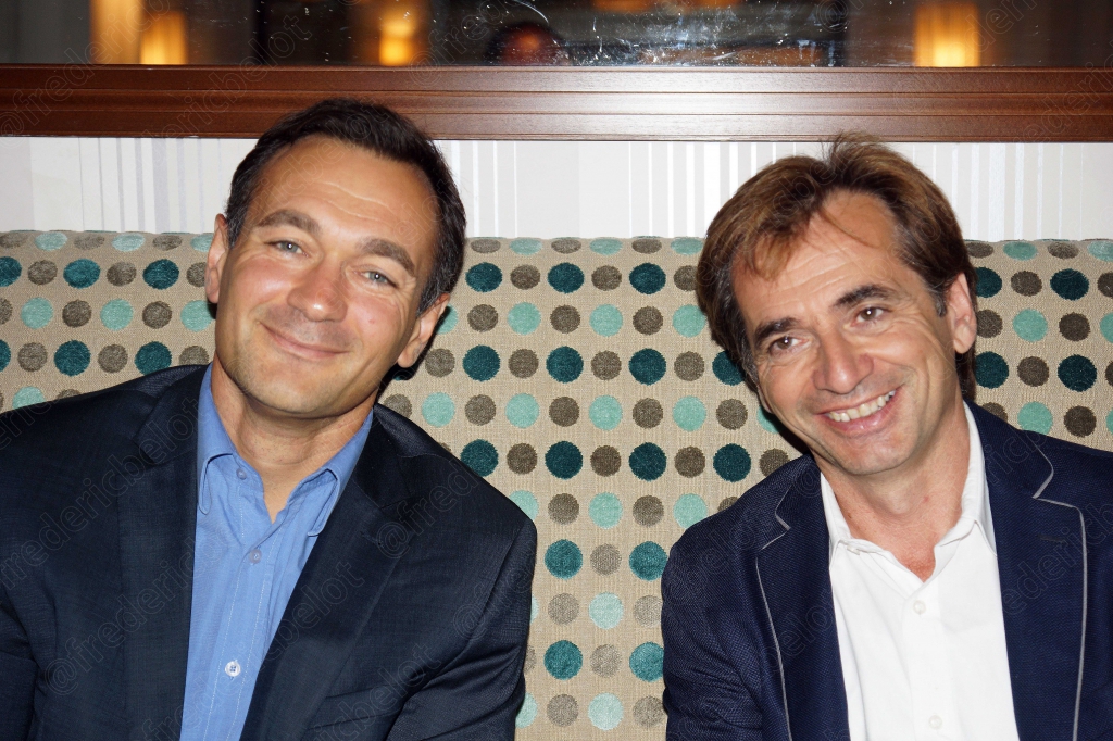Deux hommes en costume sourient côte à côte pendant le dîner.