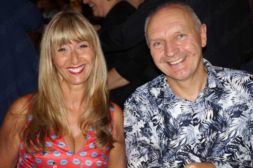 Une femme et un homme souriants posent ensemble, lui en chemise à motifs.