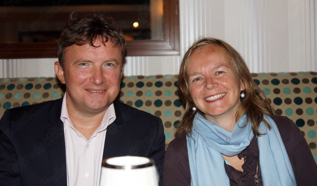 Un homme et une femme souriants posent à table, verre à la main.