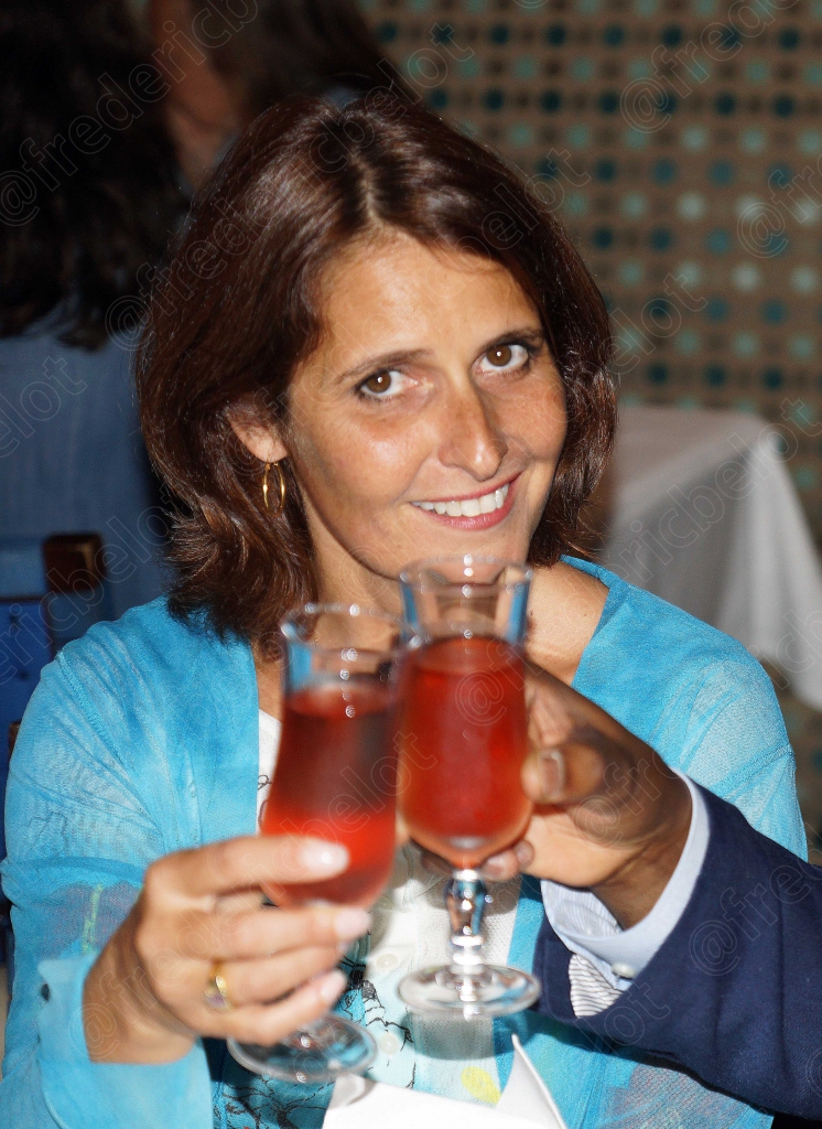 Une femme souriante lève son verre pour trinquer.