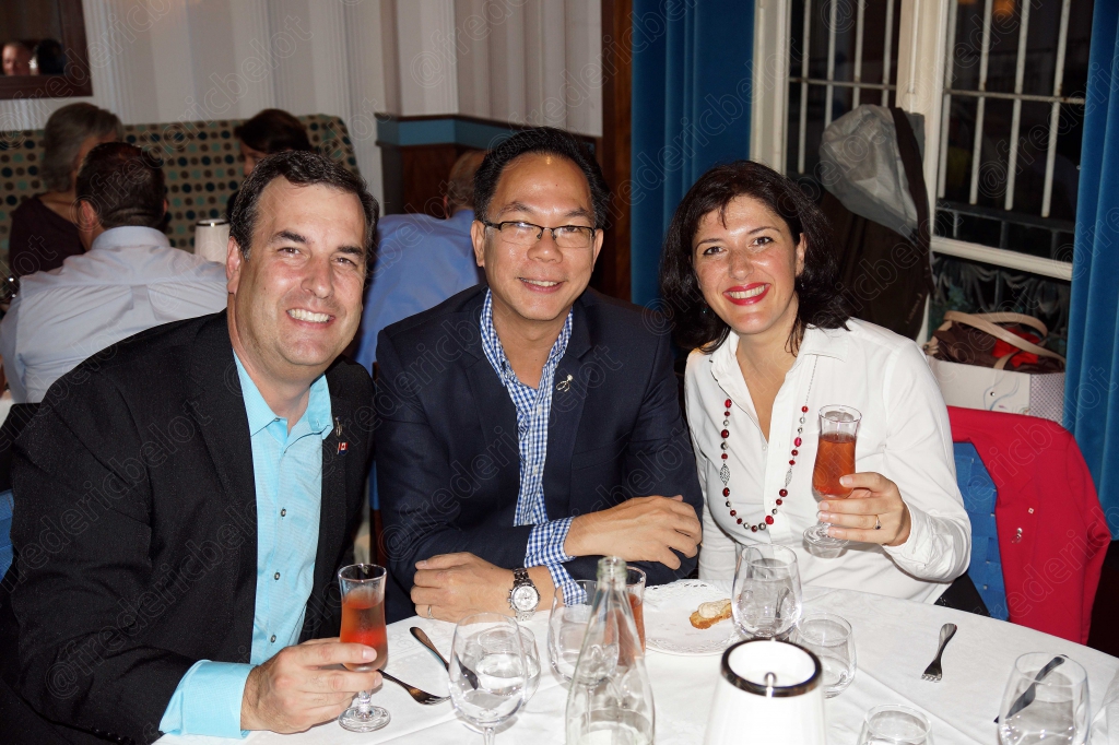 Trois convives souriants posent ensemble, verres de cocktail rouge à la main.