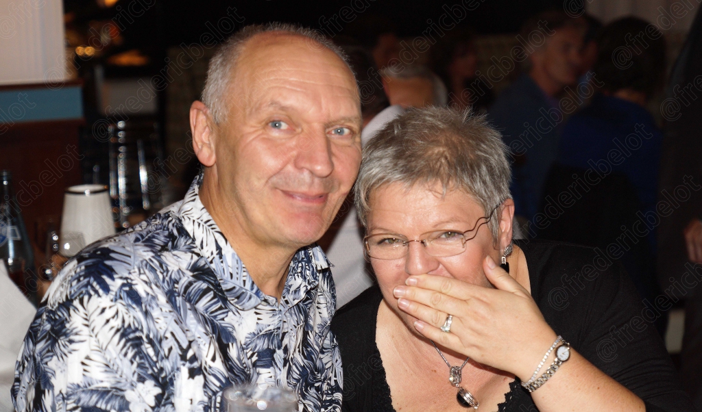 Un couple souriant pose ensemble, elle la main devant la bouche en riant.