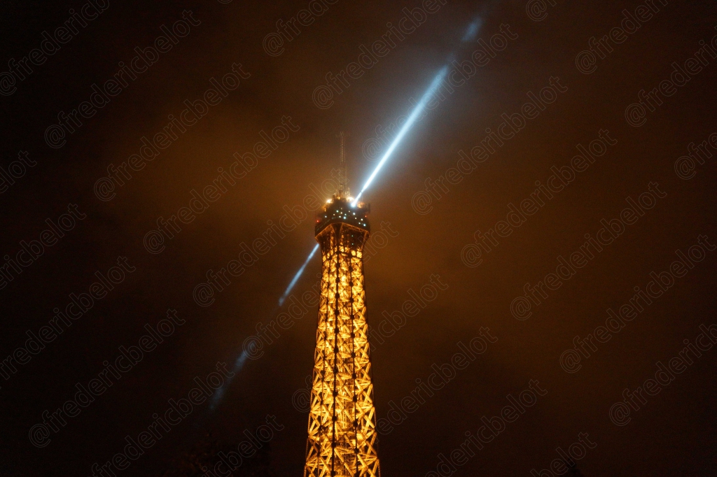 La tour Eiffel illuminée la nuit, faisceau lumineux balayant le ciel.