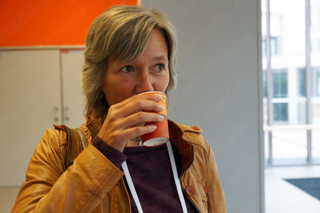 Une femme boit une boisson chaude dans un couloir vitré.