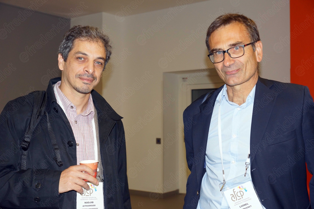 Un homme à sac à dos pose avec un homme à lunettes, souriants.