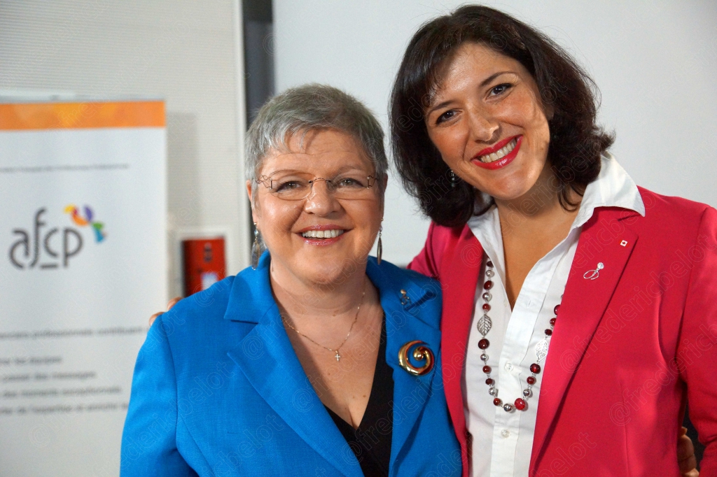 Deux femmes en veste bleue et rouge posent ensemble, souriantes, devant le kakémono AFCP.