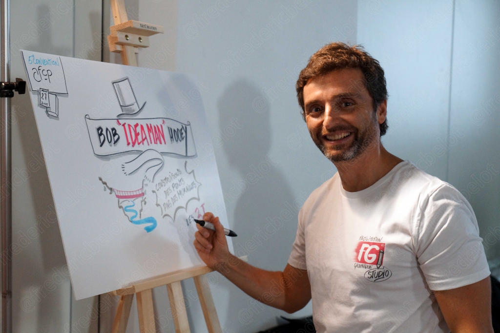 Un homme dessine une fresque murale intitulée "Bob Ideaman" sur un chevalet.