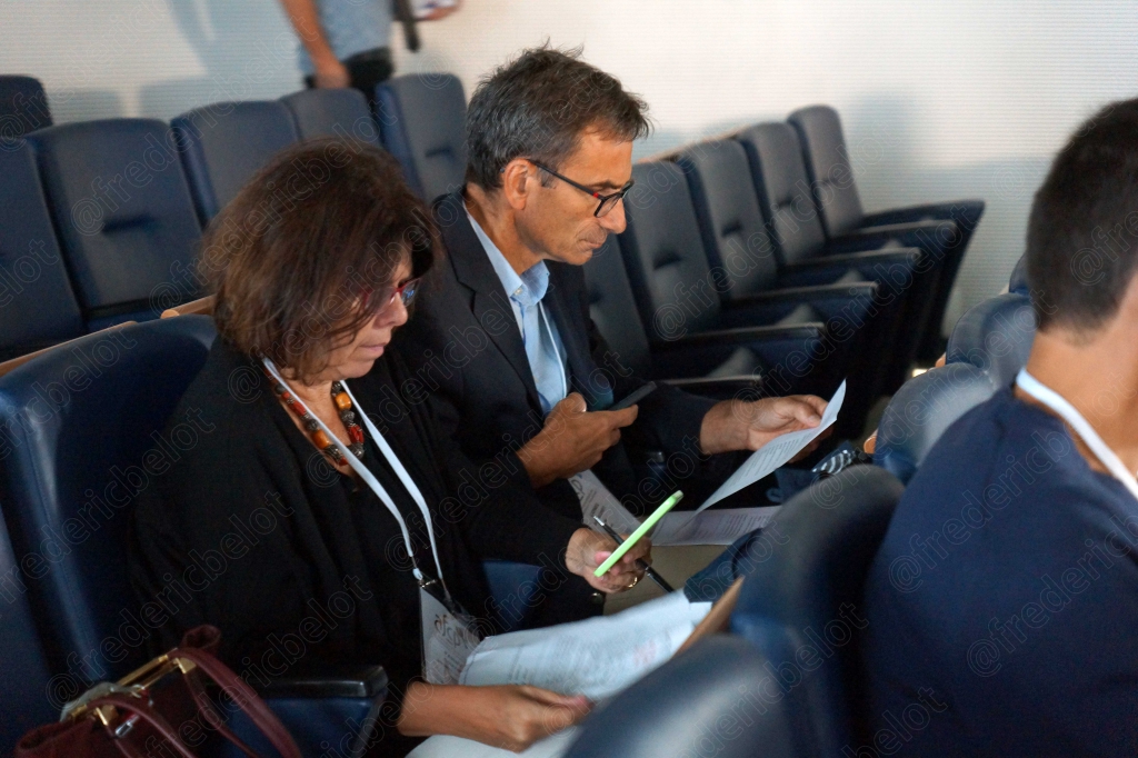 Deux personnes assises consultent des documents, dans le public.