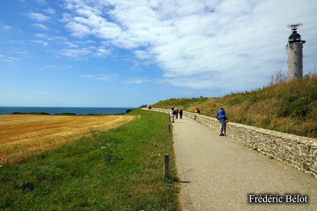 Un chemin longe le sommet de la falaise, promeneurs au loin près d'un muret de pierre.