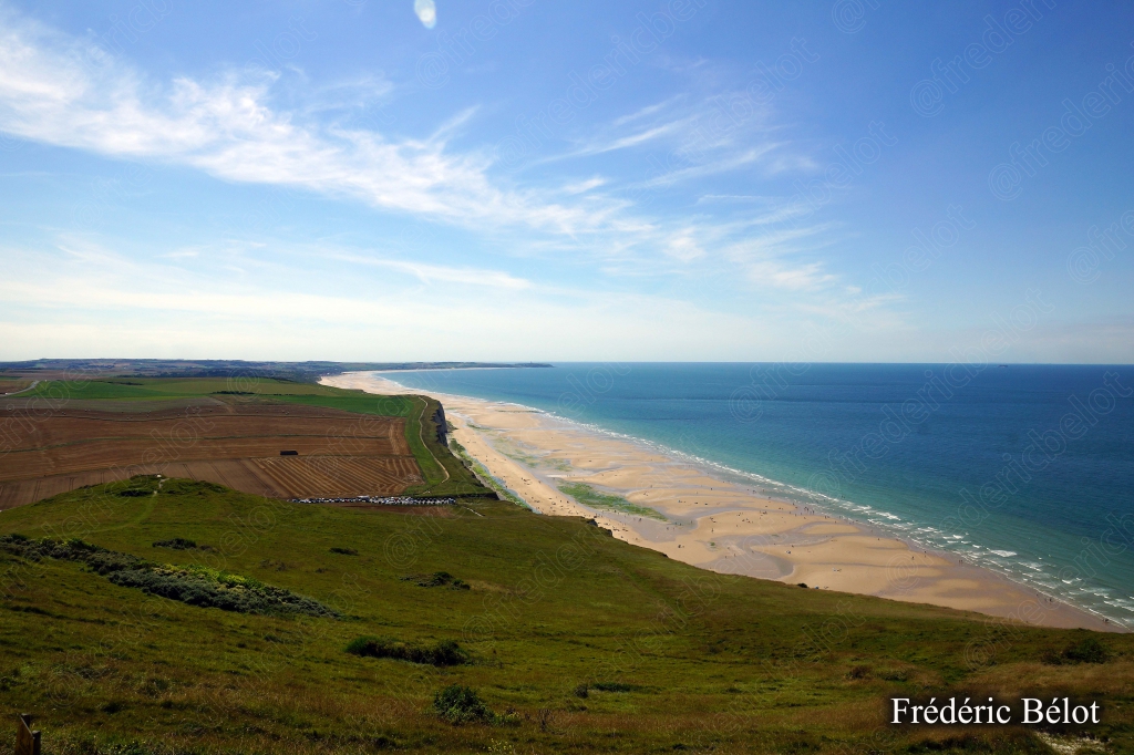 Vue plongeante sur la côte depuis le sommet de la falaise, mer et plage au loin.