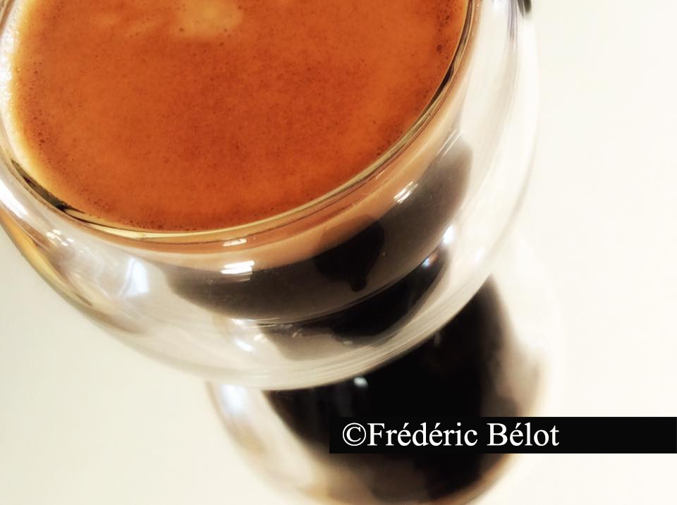 Une tasse de café noir vue de dessus, reflet de lumière à la surface.