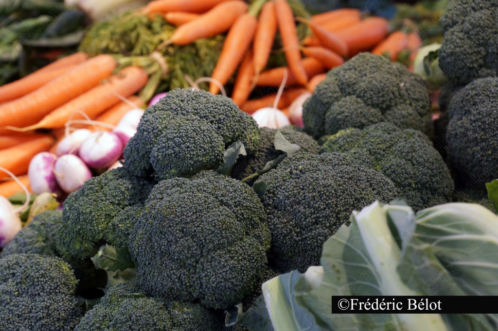 Des brocolis, radis et carottes fraîchement présentés sur un étal.