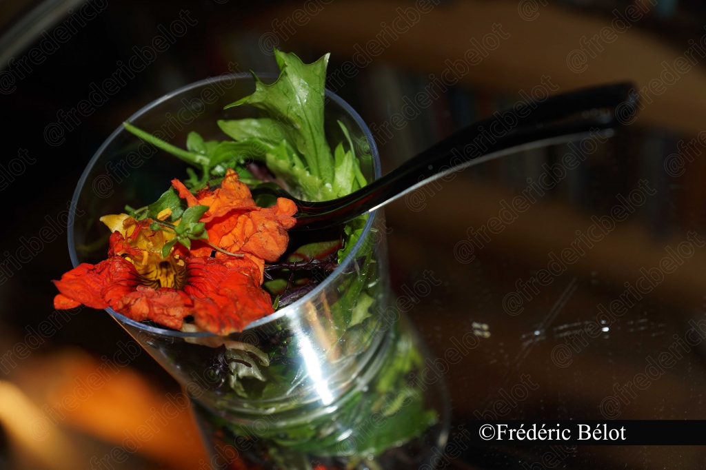 Une verrine de salade et fleurs comestibles avec une cuillère.