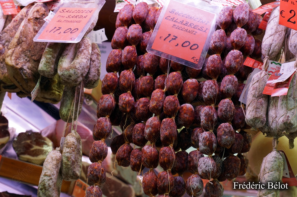 Des saucisses italiennes suspendues, étiquettes de prix rouges.