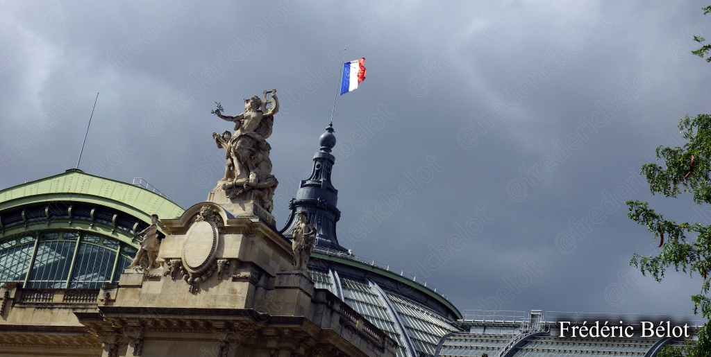 Le fronton du Grand Palais à Paris et son drapeau français, sous un ciel nuageux.