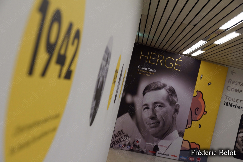 Un panneau signalétique jaune "1942" flou en premier plan, affiche Hergé à l'arrière-plan.
