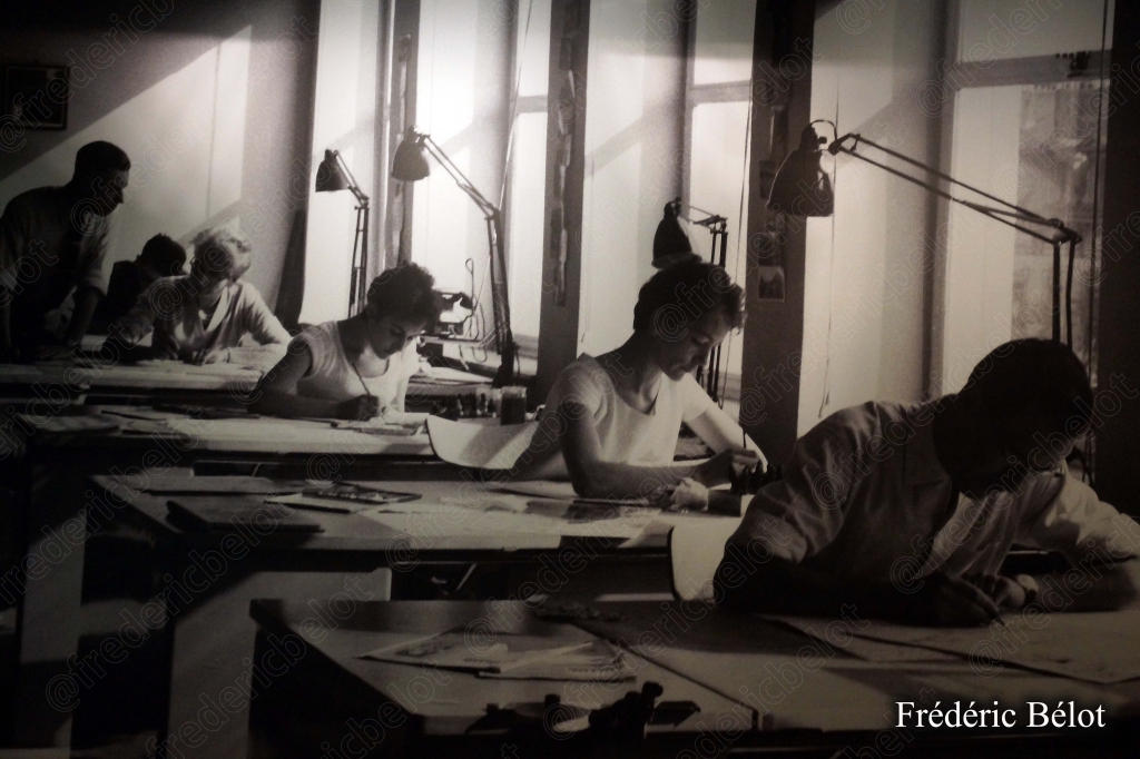 Photographie en noir et blanc d'un atelier de dessinateurs penchés sur leurs planches.