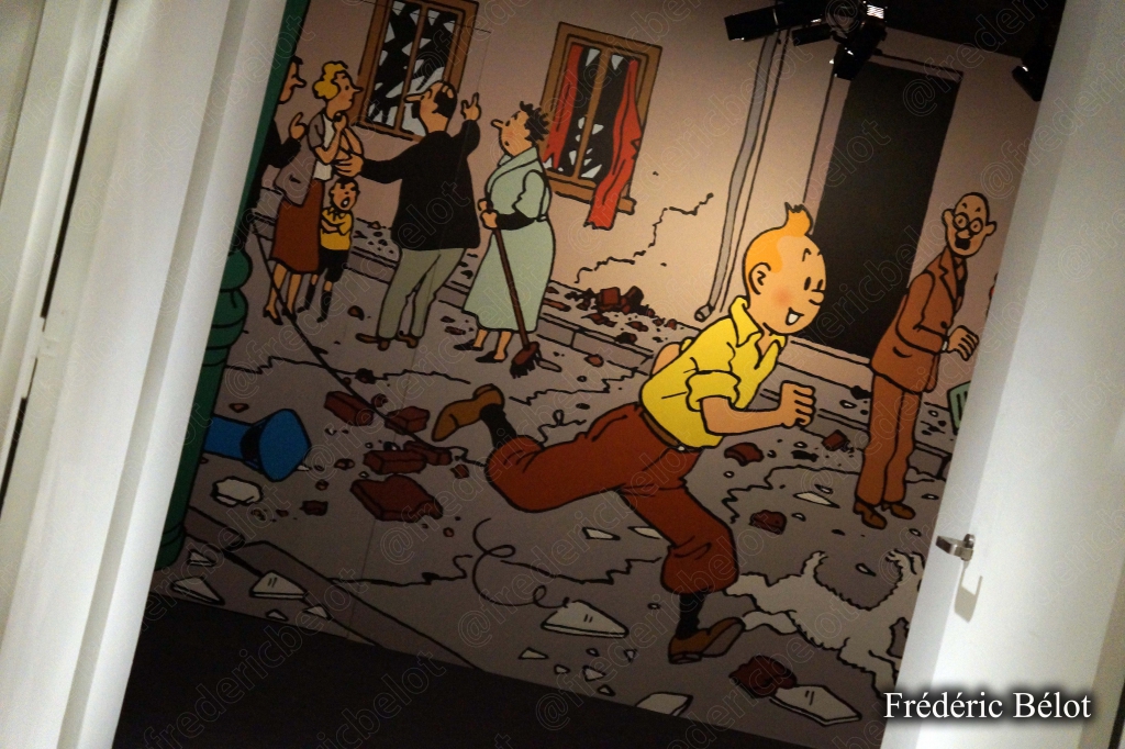 Un mur entièrement recouvert de couvertures d'albums de Tintin traduits en plusieurs langues, visiteurs de dos.