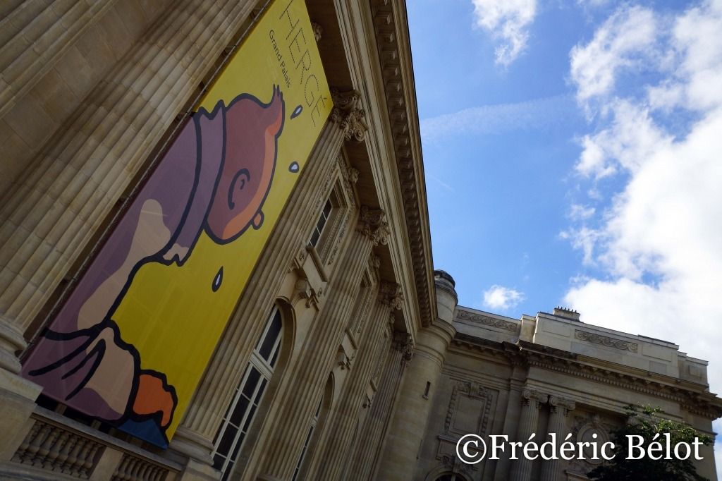 Un portrait d'Hergé projeté en lumière dorée sur un mur, enseigne "Librairie-boutique" en arrière-plan.