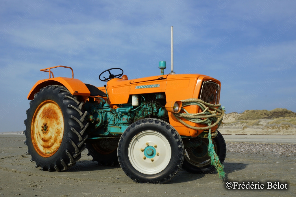 Un vieux tracteur orange stationné sur le sable, utilisé pour la mise à l'eau des bateaux.