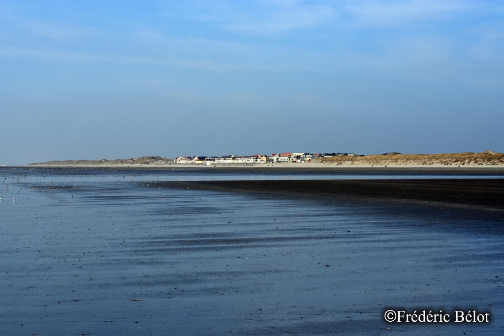 Un chenal d'eau calme reflète le ciel entre deux bancs de sable, à marée basse.