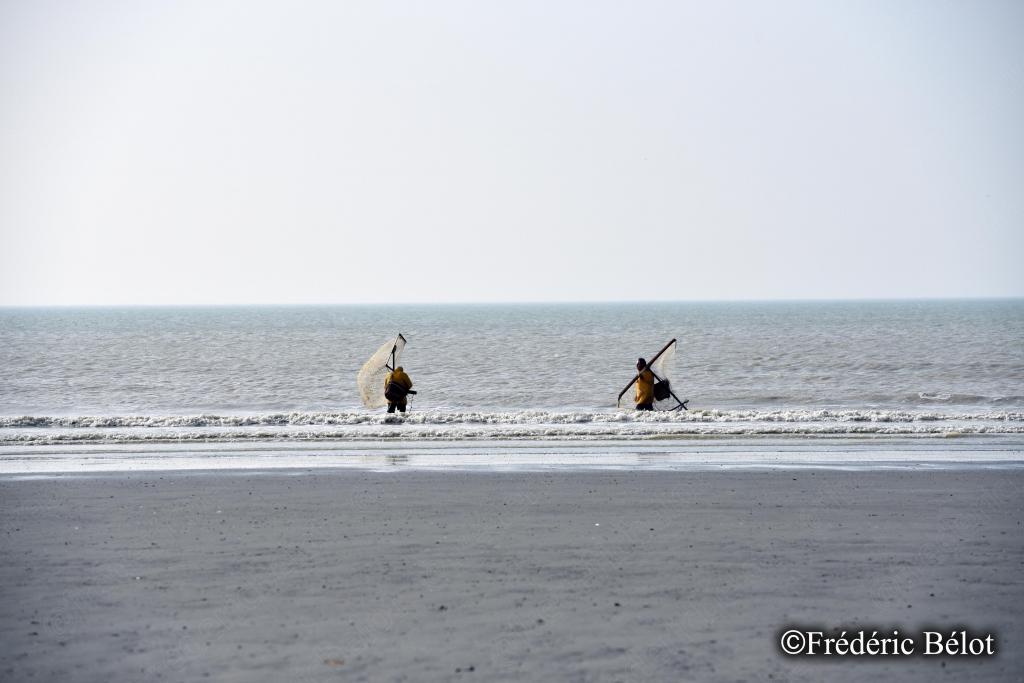 Deux pêcheurs à pied avancent avec leur haveneau dans une mer étale.