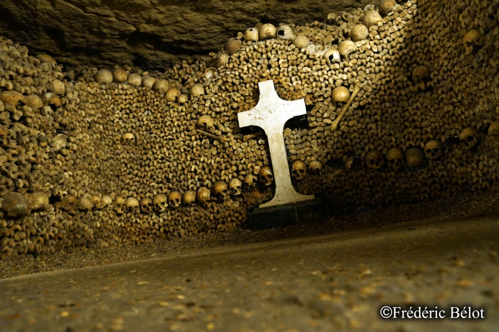 Une petite croix blanche posée devant un mur d'ossements.